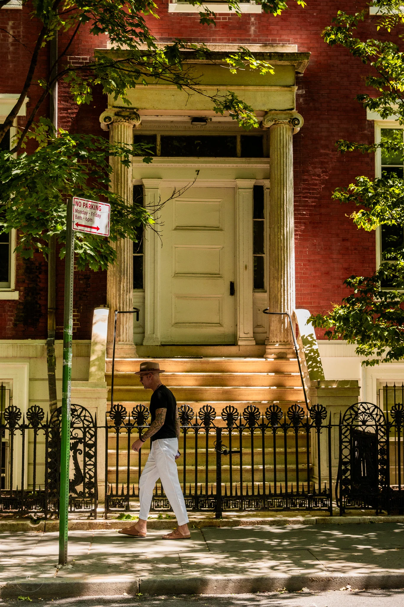 A man in a straw hat walking past a red brick townhouse with a pale green door, New York, photographed by Campbell Jensen