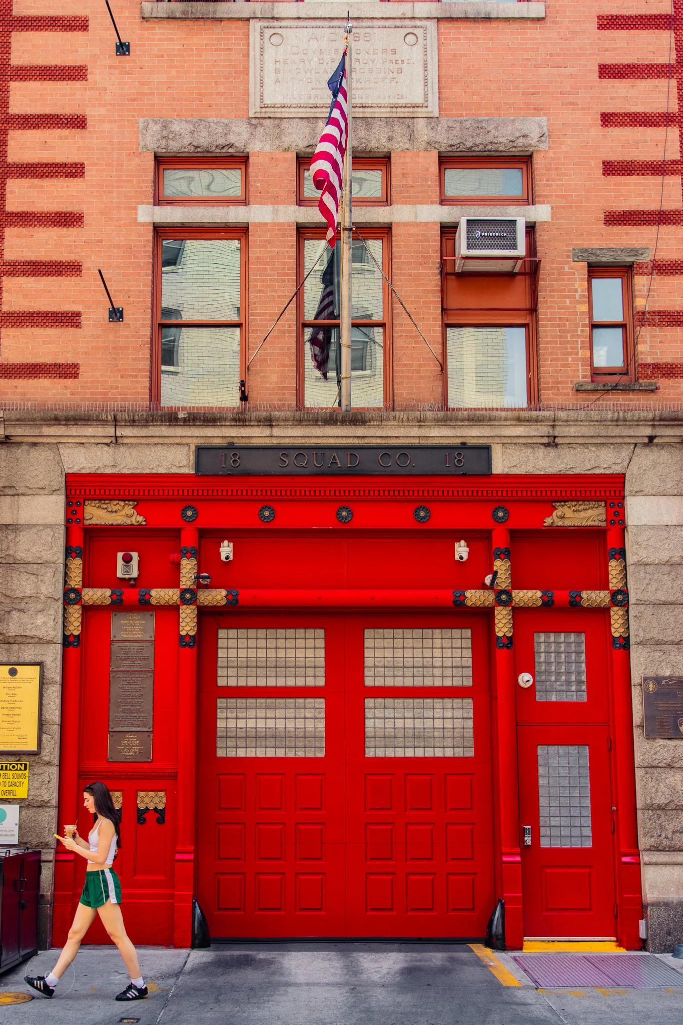 A woman walking past the red doors of Squad Company 18 firehouse, New York, photographed by Campbell Jensen